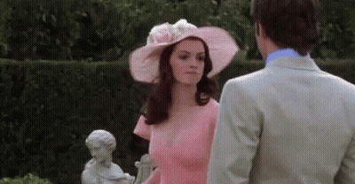 Woman In Pink Dress And Hat Next To Man In Suit GIF