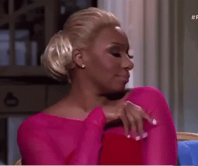 Woman In Pink Dress Sitting On Couch With Hand On Chest GIF
