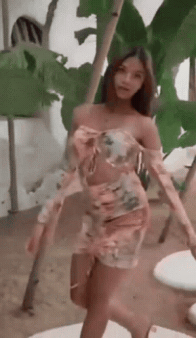 Woman In Pink Floral Dress Standing In Front Of Palm Tree GIF