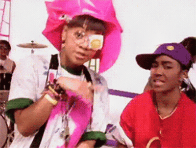 Woman In Pink Hat And Sunglasses Next To Woman In Red Shirt GIF