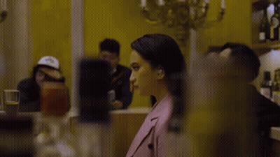 Woman In Pink Jacket Sitting At Table In Front Of Yellow Wall GIF