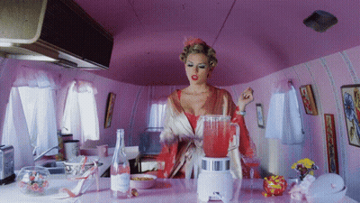 Woman In Pink Jacket Sitting At Table In Front Of Yellow Wall GIF