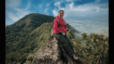 Woman In Pink Jacket Sitting On Rocky Mountain GIF