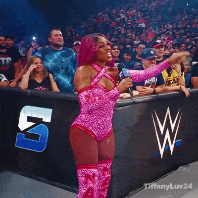 Woman In Pink Leopard Print Holding Microphone In Front Of Crowd With W Logo GIF