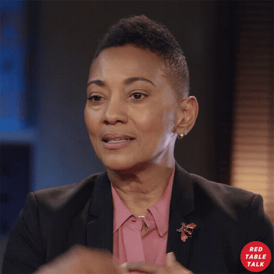 Woman In Pink Shirt And Black Jacket With Red Table Talk Logo GIF