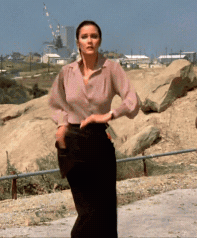 Woman In Pink Shirt And Black Pants Standing In Rocky Area GIF