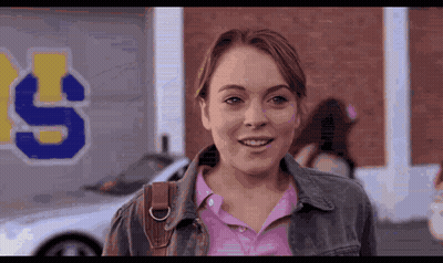 Woman In Pink Shirt And Denim Jacket Smiling In Front Of Building With Letter S GIF