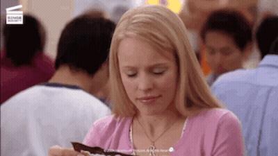 Woman In Pink Shirt Eating Chocolate In Crowded Restaurant GIF