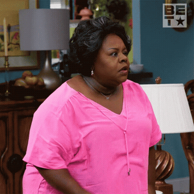 Woman In Pink Shirt Standing In Front Of Lamp And Be T Sign GIF