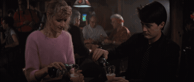 Woman In Pink Sweater Holding Beer Next To Man In Black Shirt GIF