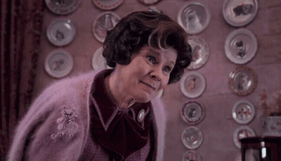 Woman In Pink Sweater In Front Of Wall With Plates GIF