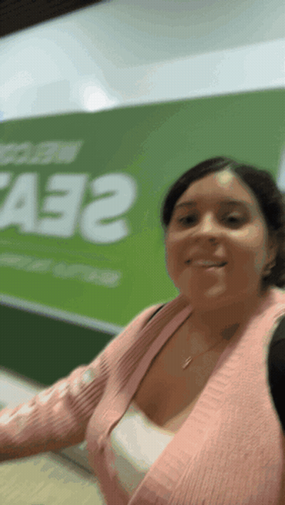 Woman In Pink Sweater Smiling In Front Of A33 Sign GIF