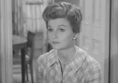 Woman In Plaid Shirt And Pearls Sitting By Door GIF