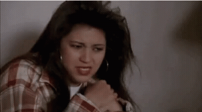 Woman In Plaid Shirt Sitting With Hand On Chest GIF
