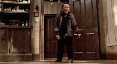 Woman In Plaid Shirt Standing In Front Of Door With Mouth Open GIF