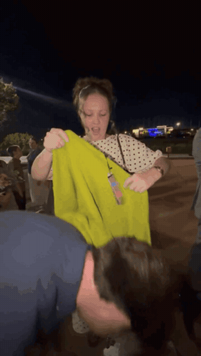 Woman In Polka Dot Shirt Holding Yellow Shirt Over Man's Head GIF
