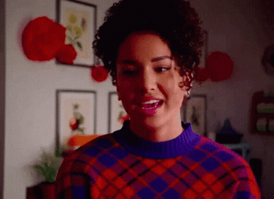 Woman In Purple And Red Plaid Sweater Smiling In Living Room GIF