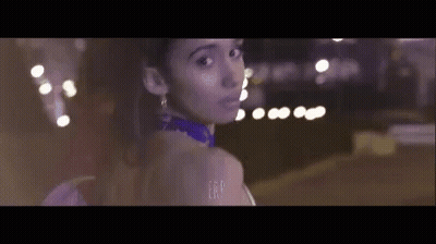 Woman In Purple Dress Standing In Front Of Blurry Lights GIF