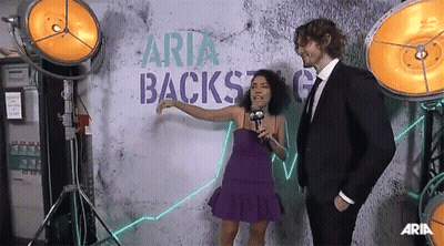 Woman In Purple Dress Talking To Man In Suit Backstage GIF
