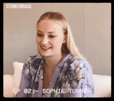 Woman In Purple Floral Shirt Smiling On Couch GIF