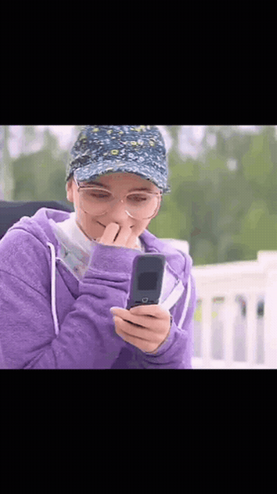 Woman In Purple Hoodie And Hat Looking At Phone GIF
