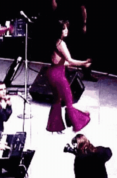 Woman In Purple Jumpsuit Dancing On Stage While Man Takes Photo GIF