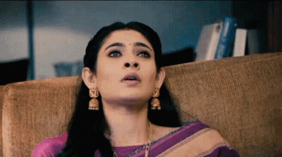 Woman In Purple Saree And Gold Earrings Sitting On Couch GIF