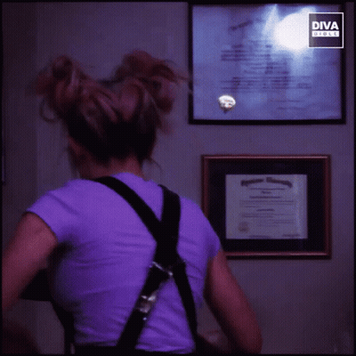Woman In Purple Shirt And Black Overalls Smiling In Front Of Diva Screen GIF