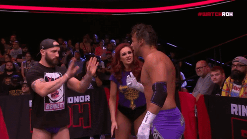Woman In Purple Shirt With Cross Next To Man In Purple Shorts GIF