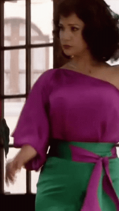 Woman In Purple Top And Green Pants Standing By Window GIF