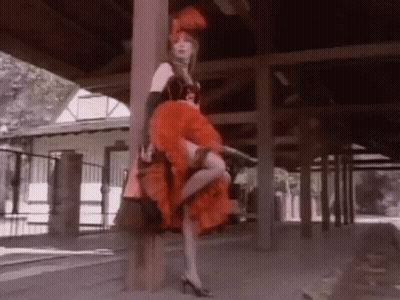 Woman In Red Can Can Dress Standing By Wooden Post GIF