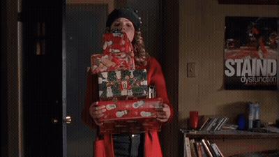 Woman In Red Coat Holding Christmas Presents In Front Of Staind Dysfunction Poster GIF