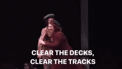 Woman In Red Coat On Stage Before Man In Brown Jacket GIF