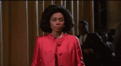 Woman In Red Coat Standing In Front Of Curtain GIF