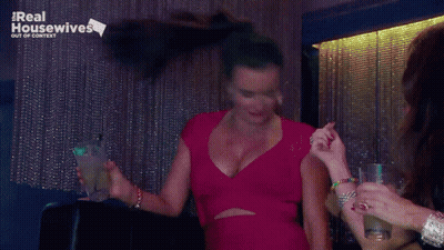 Woman In Red Dress Holding Drink In Front Of Real Housewives Sign GIF