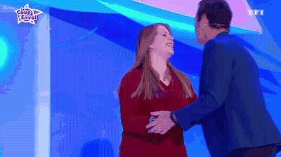 Woman In Red Dress Hugging Man In Blue Suit In Front Of Coup D'Envo Sign GIF