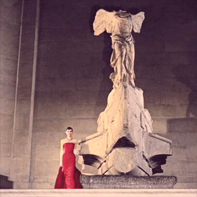 Woman In Red Dress Next To Statue GIF