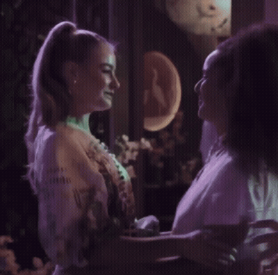 Woman In Red Dress Next To Woman In White Coat GIF