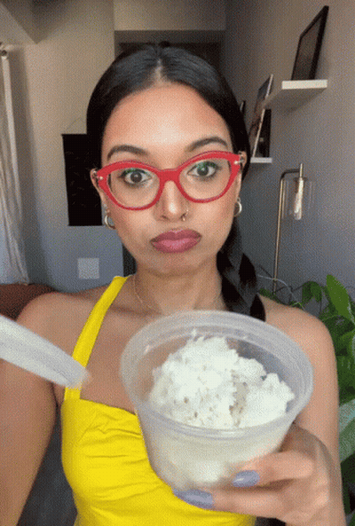 Woman In Red Glasses And Yellow Top Holding Food Container GIF
