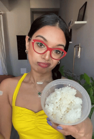Woman In Red Glasses And Yellow Top Holding Rice Container GIF