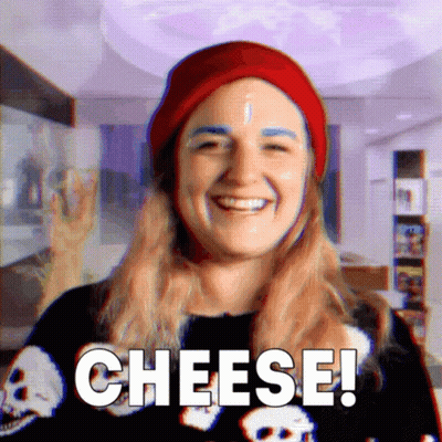Woman In Red Hat And Skull Shirt Saying Cheese GIF
