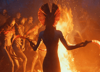 Woman In Red Headdress Standing In Front Of Fire GIF