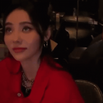 Woman In Red Jacket And Earrings Sitting In Dark Room GIF