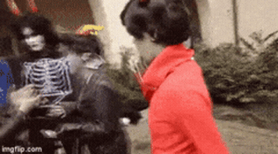 Woman In Red Jacket Next To Skeleton Costume GIF