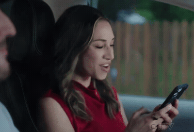 Woman In Red Shirt Sitting In Back Seat Looking At Phone GIF
