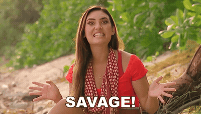 Woman In Red Shirt Sitting On Beach With Hands Outstretched Saying Savage GIF
