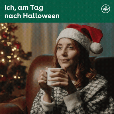 Woman In Santa Hat Sitting On Couch Holding Coffee GIF