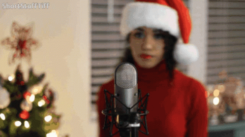 Woman In Santa Hat Standing In Front Of Microphone GIF