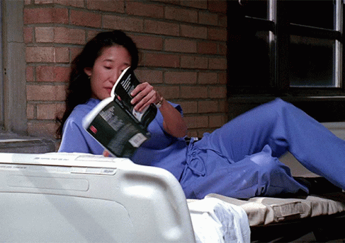 Woman In Scrubs Lying On Bed Reading Magazine GIF