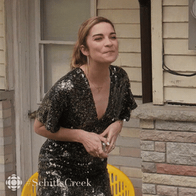 Woman In Sequined Dress Sitting In Front Of Brick Building Schitts Creek GIF